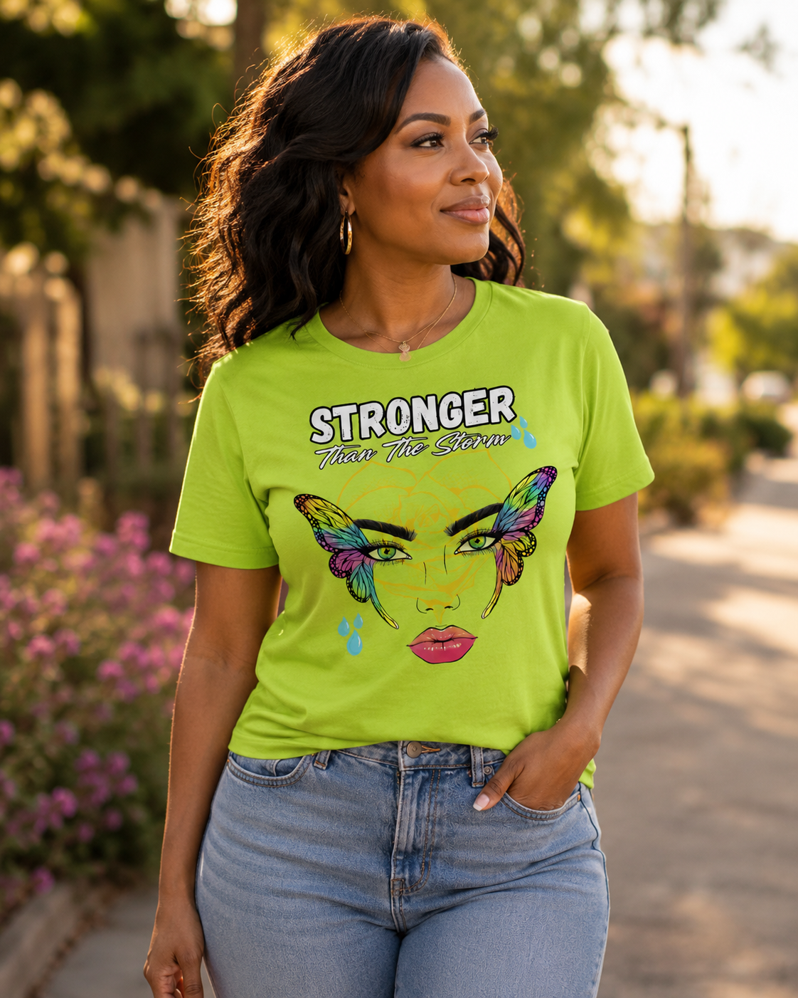 Woman wearing a lime green “Stronger Than the Storm” graphic tee outdoors in warm golden sunlight with a calm, confident expression.